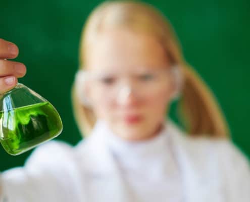 girl student with a chemistry beaker in her hand filled with green, and a chalkboard background