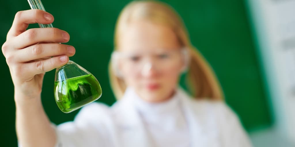 girl student with a chemistry beaker in her hand filled with green, and a chalkboard background