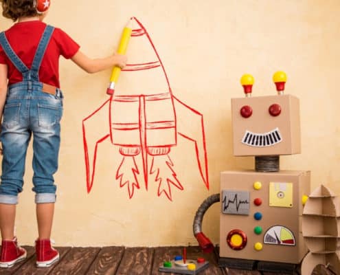 boy child with a cardboard robot, drawing a spaceship on the wall