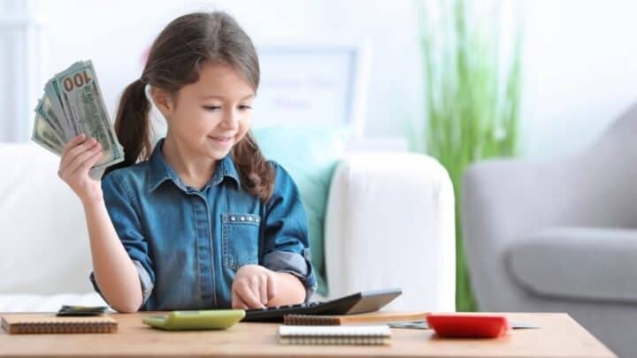 young girl with hand of money and smiling, using calculator at desk