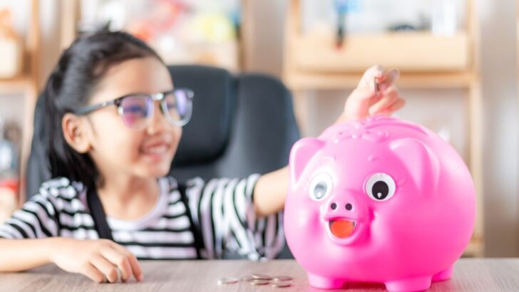 preschool girl with glasses putting money into piggy bank