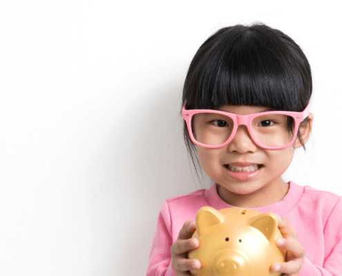 little girl with pink glasses holding a piggy bank, waiting for personal finance homeschool lessons