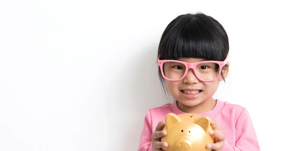 little girl with pink glasses holding a piggy bank, waiting for personal finance homeschool lessons