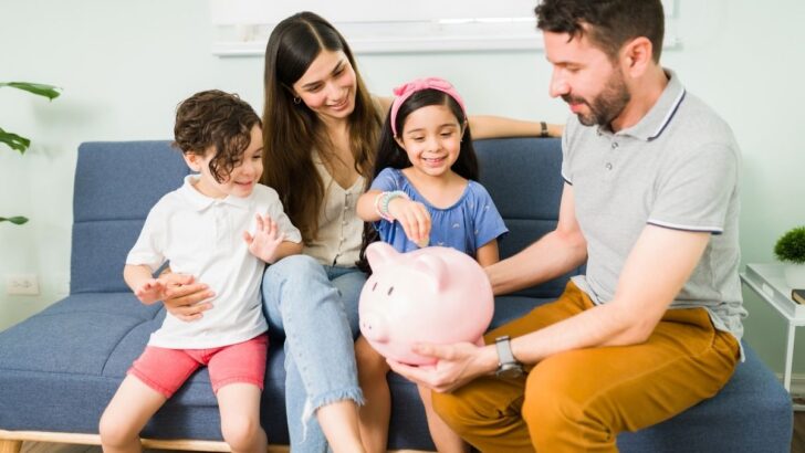 family sitting on sofa, father holding piggy bank and talking family money values