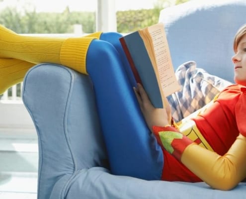 child in superman outfit on couch reading books about money for kids