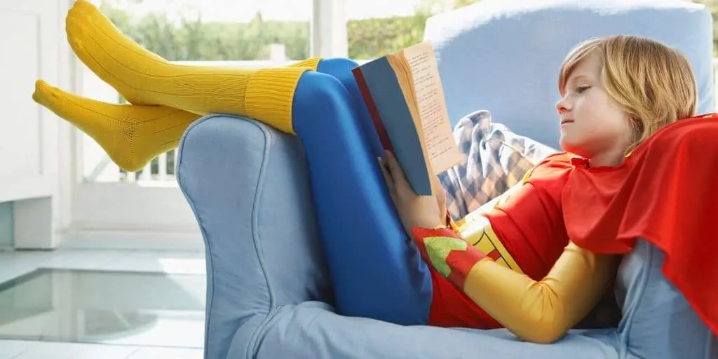 child in superman outfit on couch reading books about money for kids