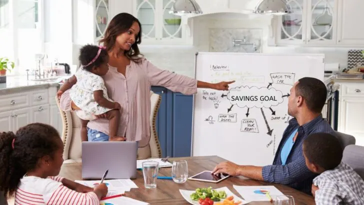 family around kitchen table with white board showing family savings goal