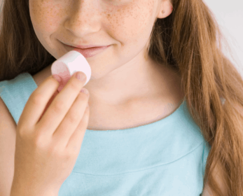 Girl holding a marshmallow to her mouth, looking like she might eat it, with a smile