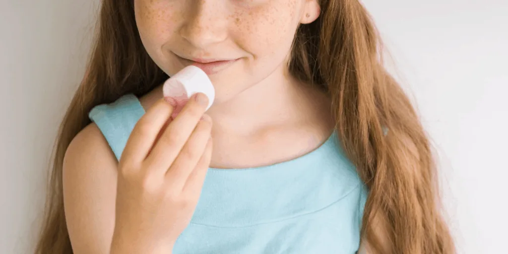 Girl holding a marshmallow to her mouth, looking like she might eat it, with a smile