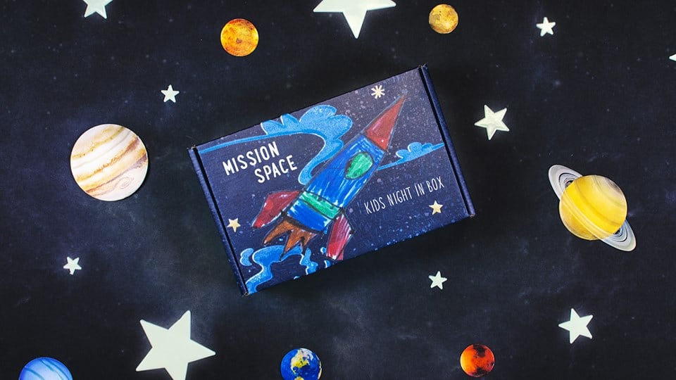 box with a rocket ship on it drawn by a kid, with stars and planets on background