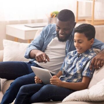 father and son looking at allowance tracking app on tablet, smiling at the screen