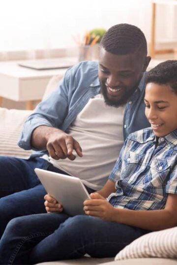 father and son looking at allowance tracking app on tablet, smiling at the screen