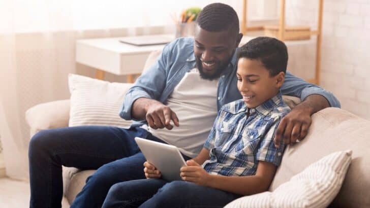 father and son looking at allowance tracking app on tablet, smiling at the screen