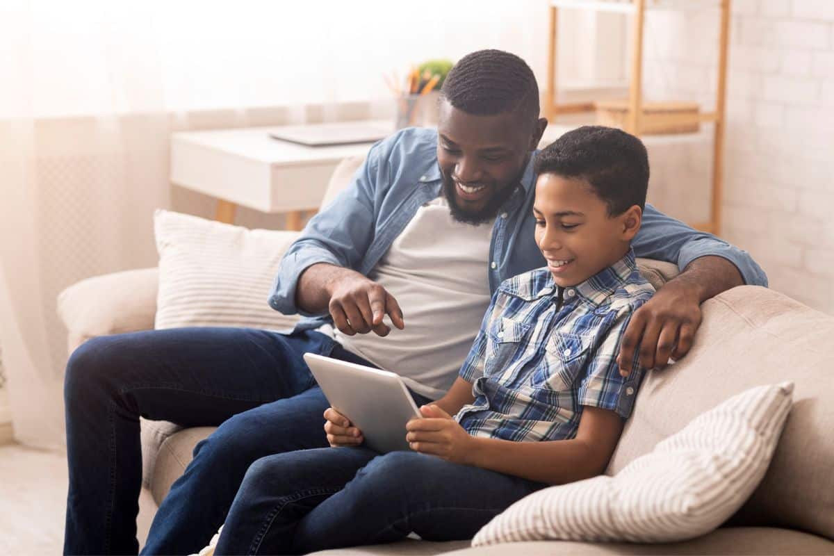 father and son looking at allowance tracking app on tablet, smiling at the screen