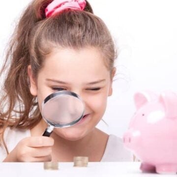 tween girl with magnifying glass looking at money and piggy bank