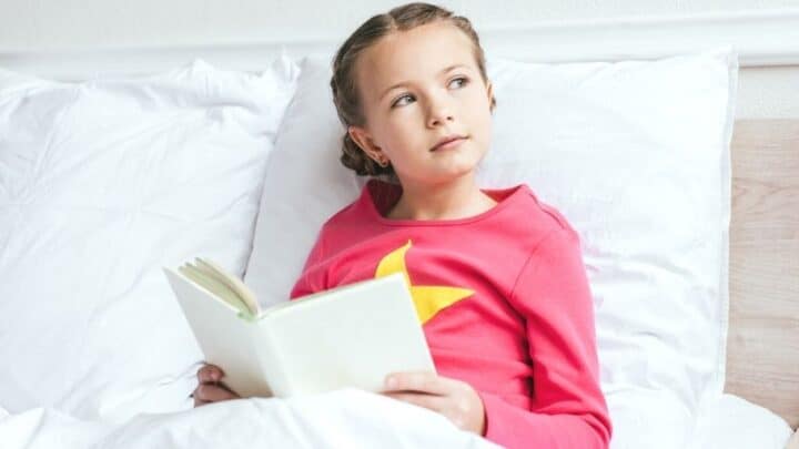 young girl kid in bed reading business book for kids, looking off into distance
