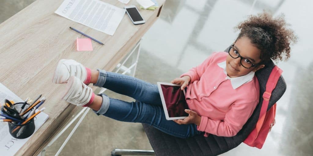 kid entrepreneur sitting in business chair at desk, black glasses, looking up at camera