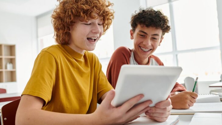 two tween boys smiling at banking activity on ipad in classroom