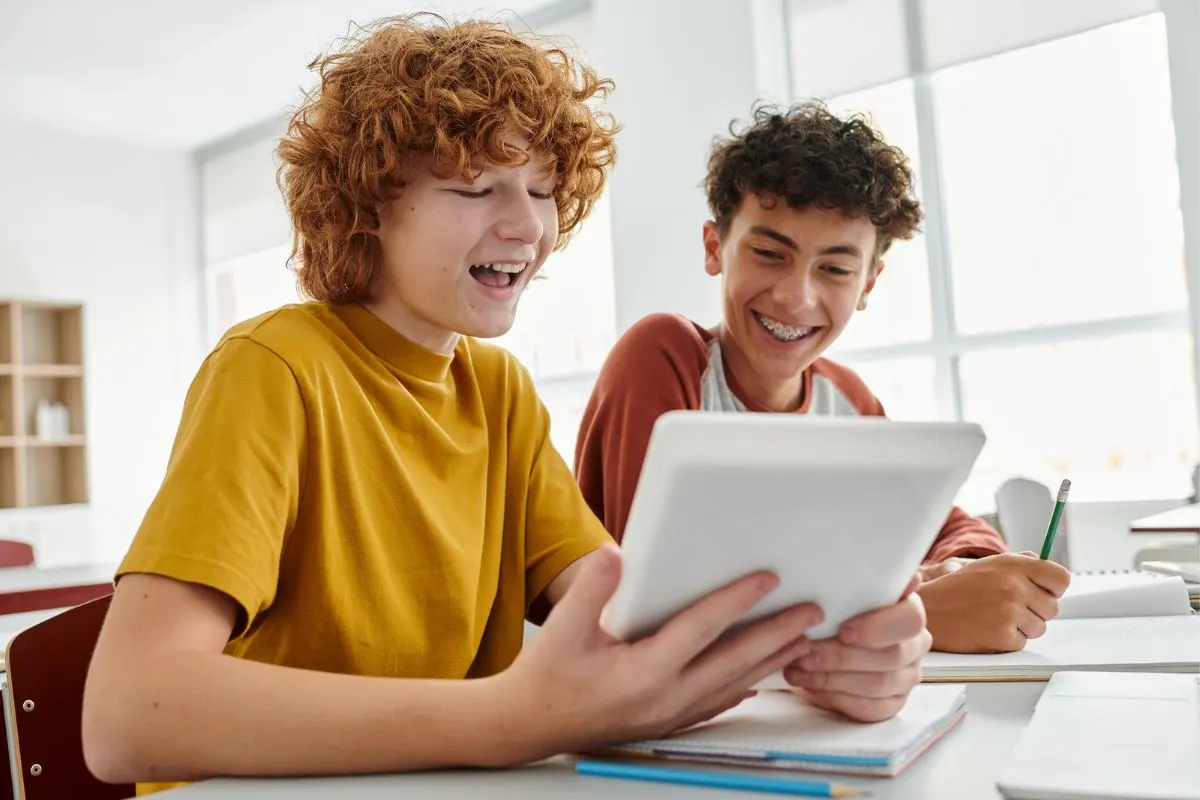 two tween boys smiling at banking activity on ipad in classroom