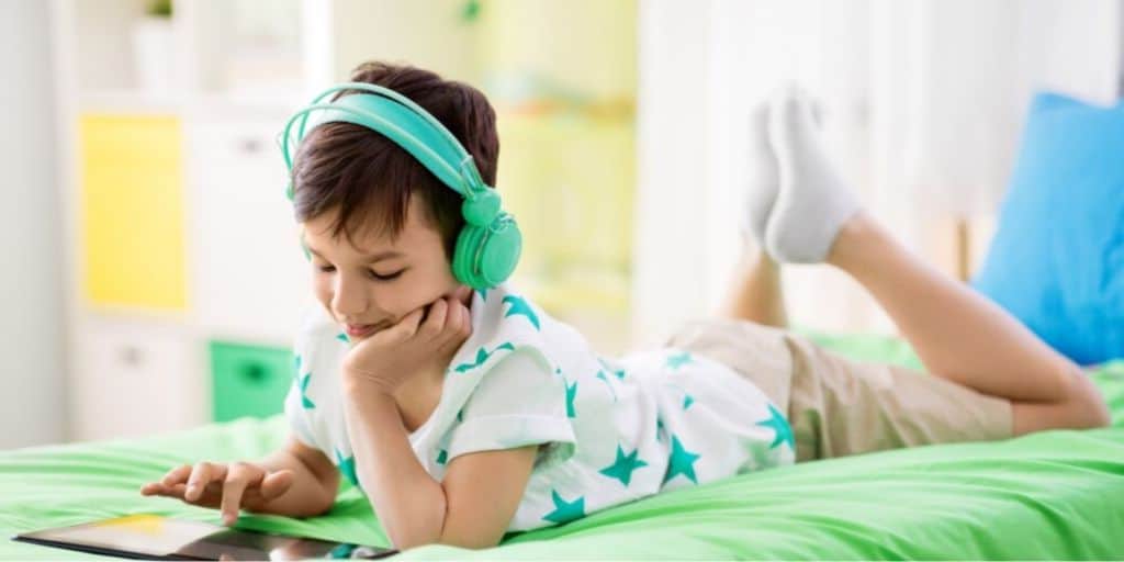 young boy laying on bed with iPad playing a math money app