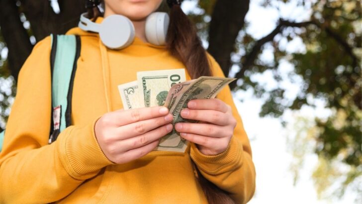 teen in yellow hoodie with headphones, holding cash