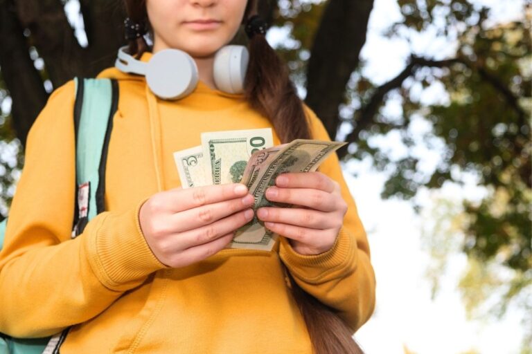 teen in yellow hoodie with headphones, holding cash