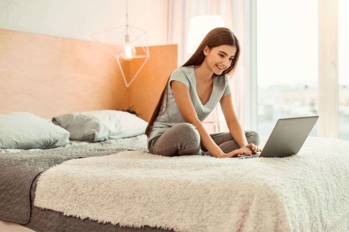 girl teen on bed with laptop, smiling