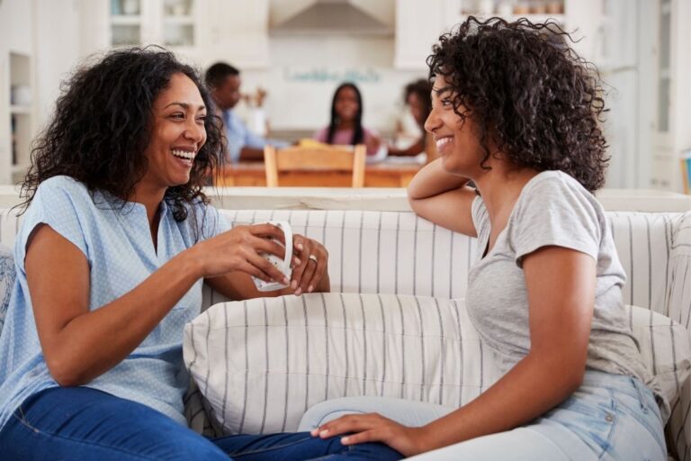 mother talking to teenage daughter on sofa, both smiling