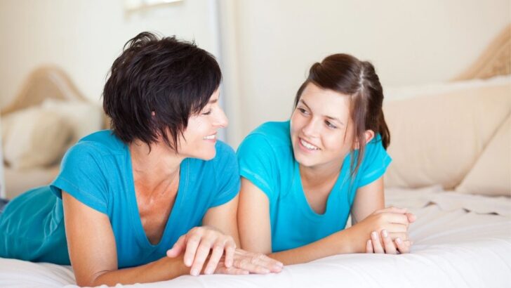 mom and teen daughter talking on bed in blue shirts