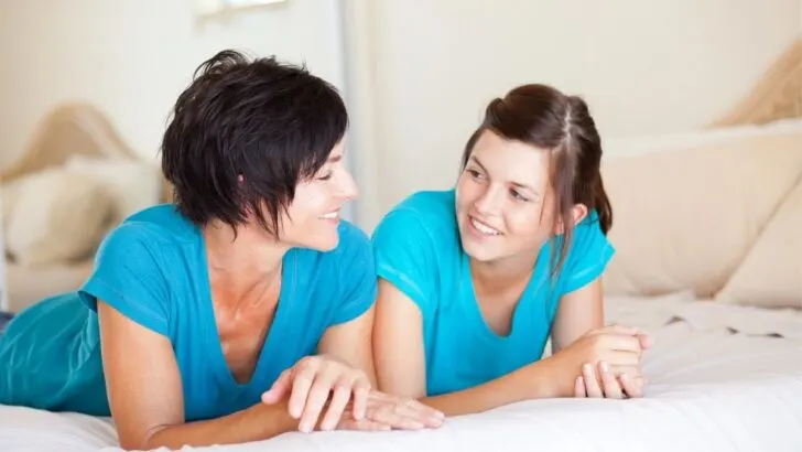 mom and teen daughter talking on bed in blue shirts