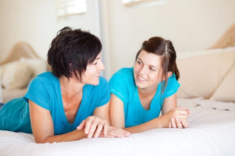 mom and teen daughter talking on bed in blue shirts