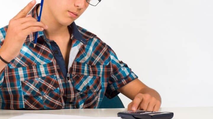 teen boy with calculator and pencil on desk filling in a budget worksheet for students