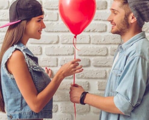 teenage couple holding a red balloon, girl giving high school valentines day gifts for him