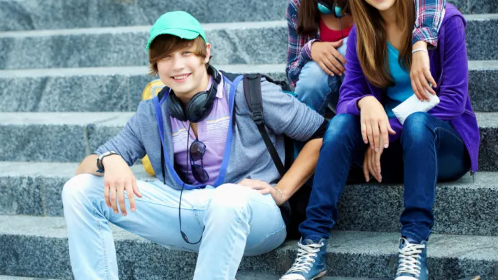 teenage guy sitting on stone steps with two teen girls, wearing headphones