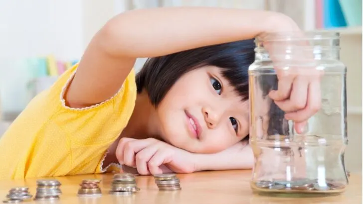 girl counting coins and adding to mason jar piggy bank