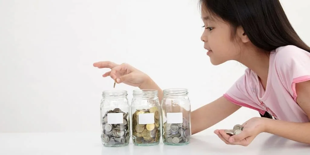 young Asian girl counting coins in three jars
