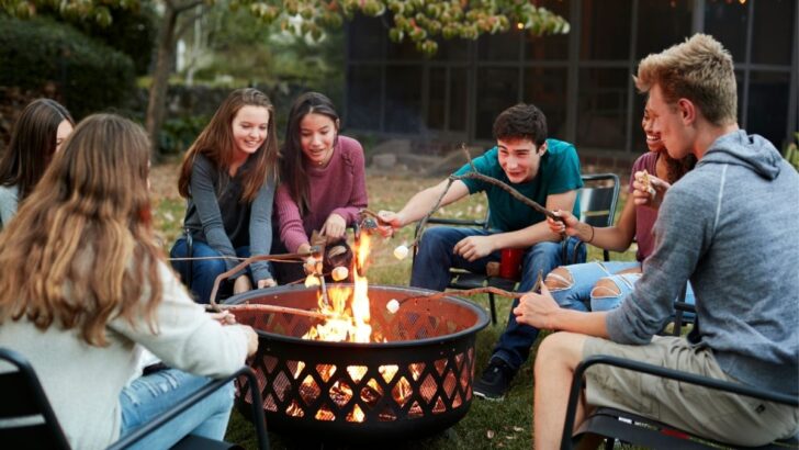 group of teens double date in backyard fire pit making s'mores