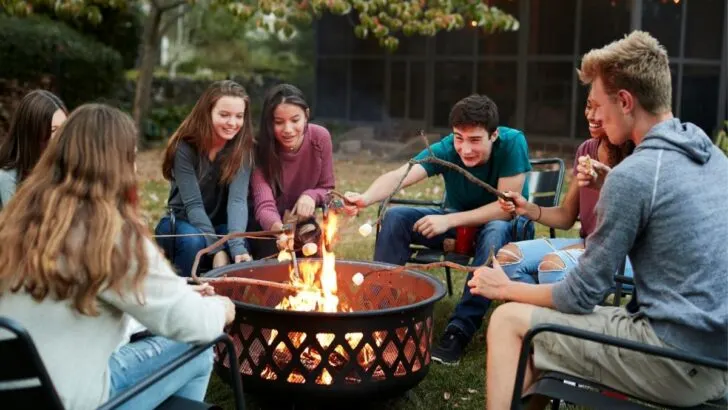 group of teens double date in backyard fire pit making s'mores