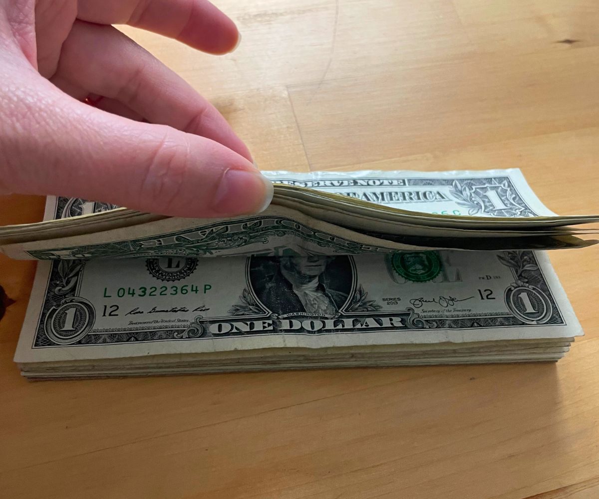 hand thumbing through DIY money notepad (all $1 bills)