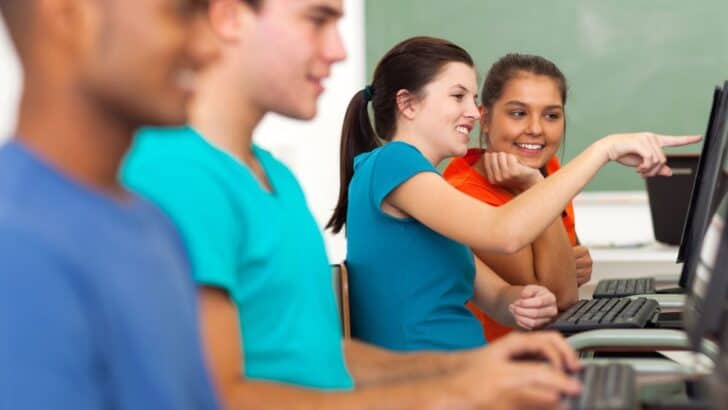 row of four teen students in front of computers, smiling, playing financial literacy game