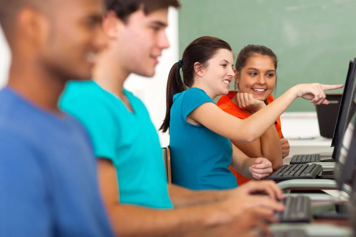 row of four teen students in front of computers, smiling, playing financial literacy game