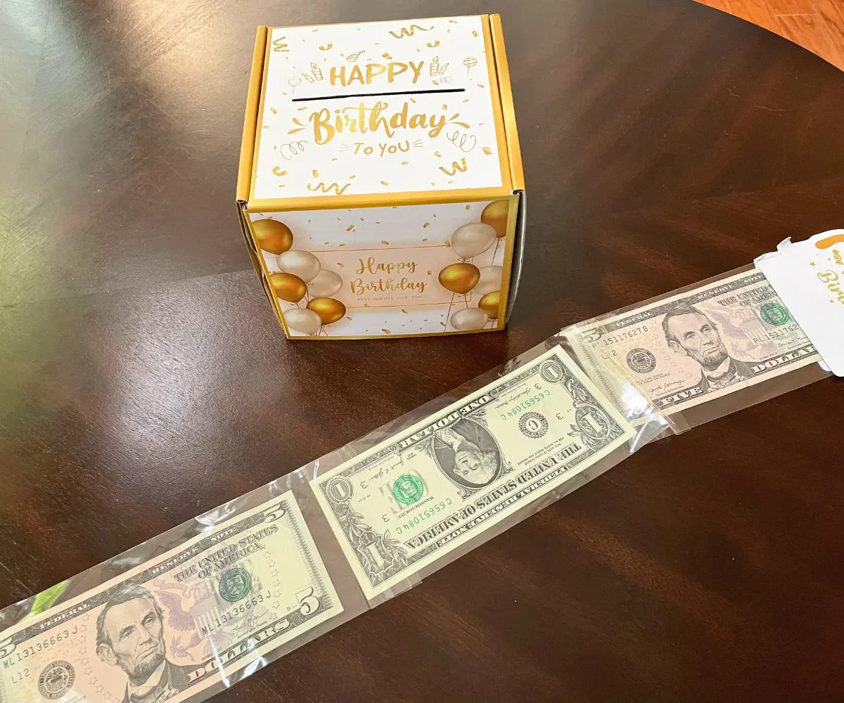 gold and white birthday cash box with long train of dollar and five-dollar bills in plastic along the front