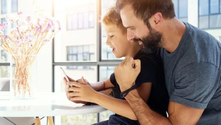 father looking over son's shoulder who's learning stock market stuff on iPhone