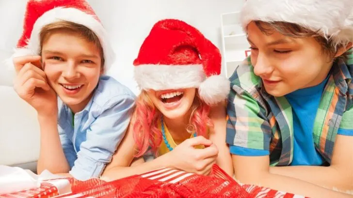 two tween boys with tween girl in Santa hats, goofing around