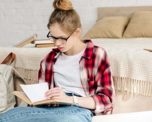 young teen woman with dark glasses on floor, reading financial literacy books for high school students