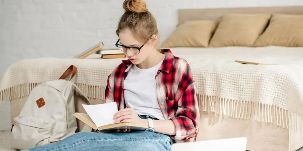 young teen woman with dark glasses on floor, reading financial literacy books for high school students