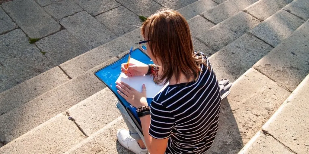 teen girl sitting on school steps with after school schedule at home on clipboard, writing