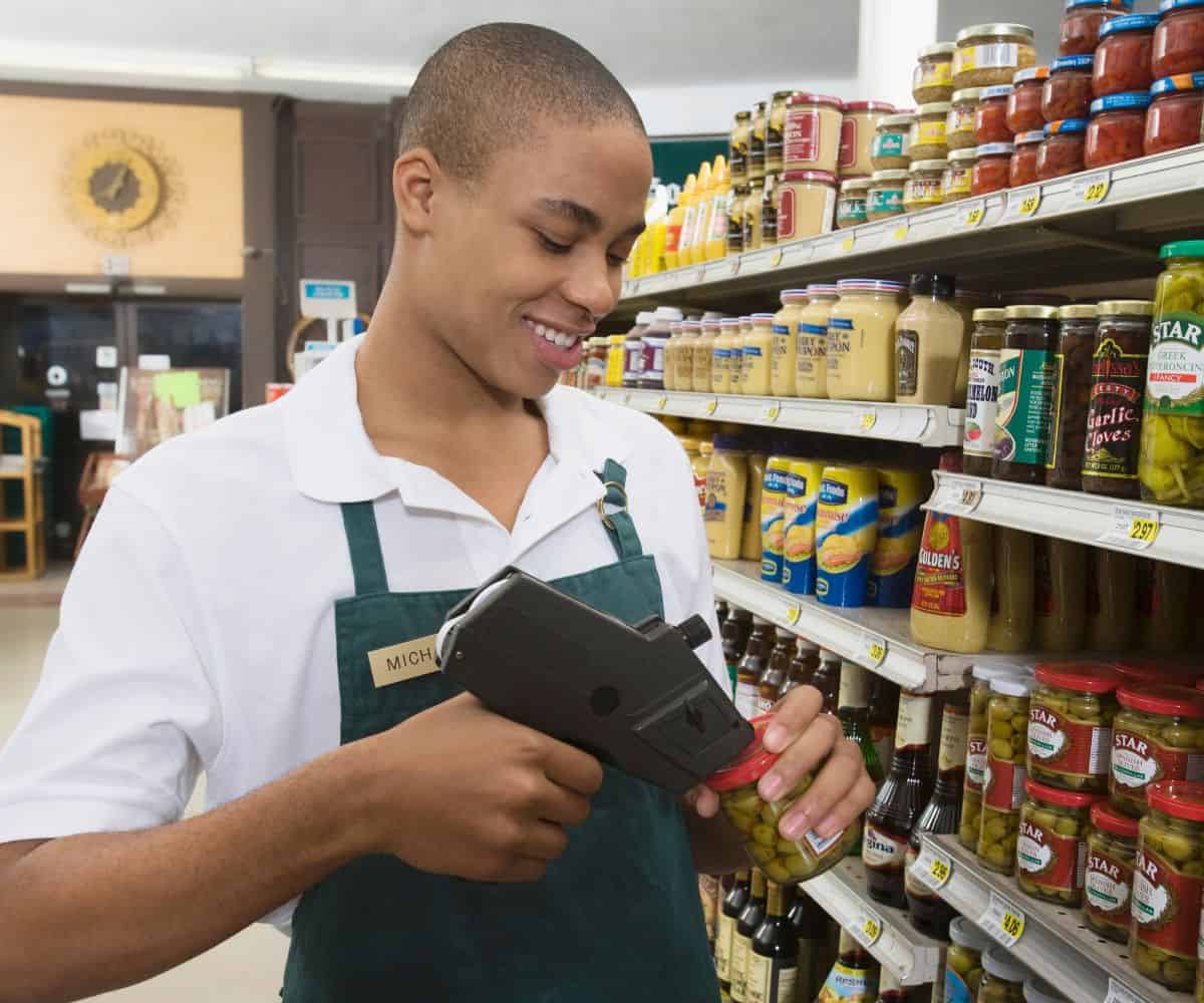 teen boy pricing top of olive jar at grocery store