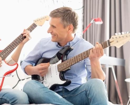 father playing guitar with teenage daughter as a family activity with teen