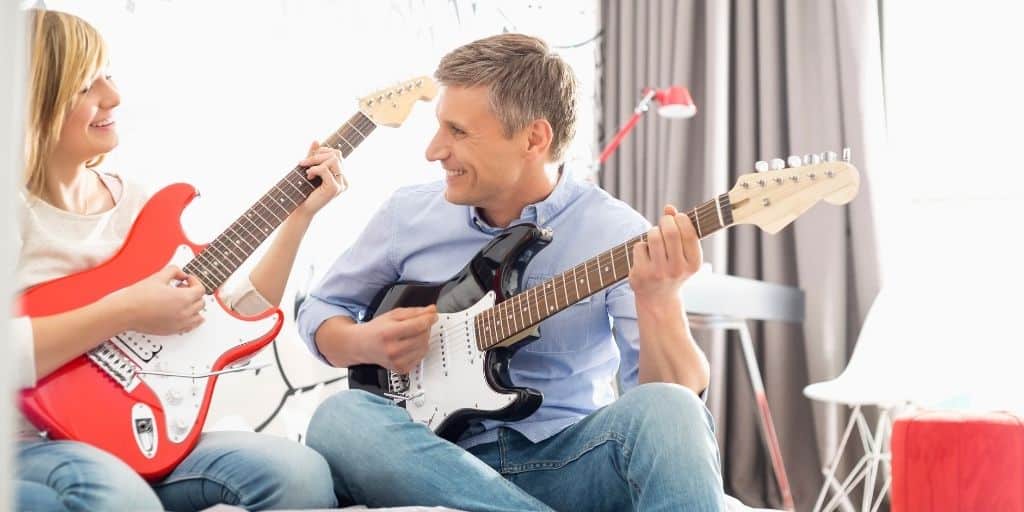 father playing guitar with teenage daughter as a family activity with teen